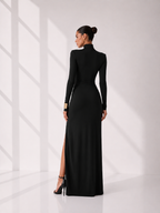 Woman wearing a black long-sleeve gown with a high slit on a white background