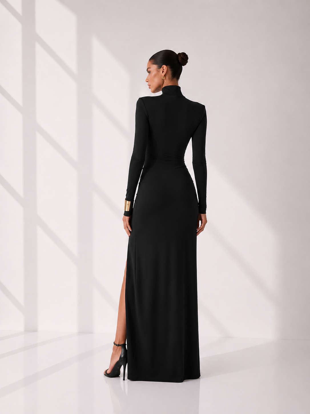 Woman wearing a black long-sleeve gown with a high slit on a white background