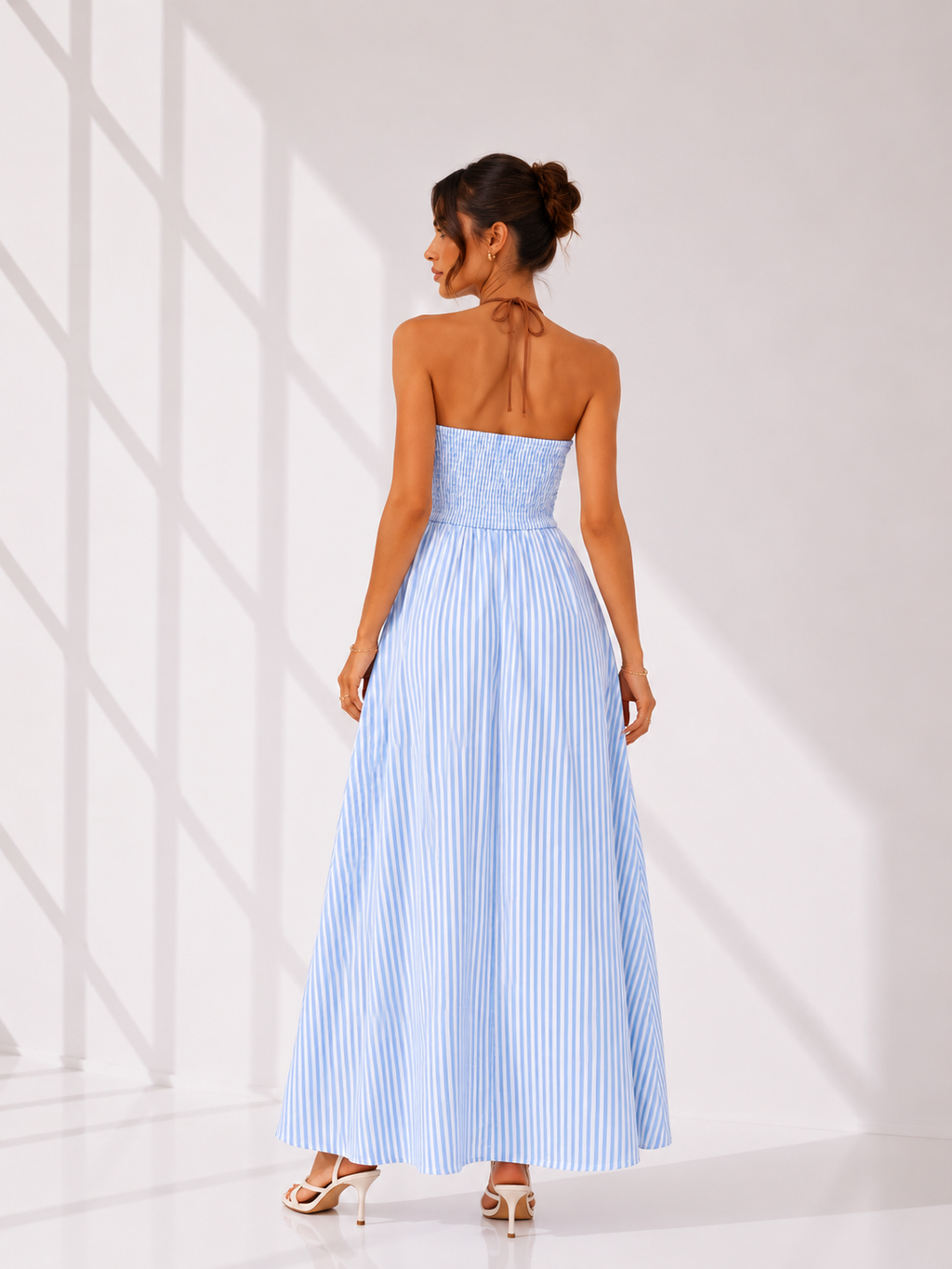 Woman wearing a light blue strapless dress with vertical stripes against a white background