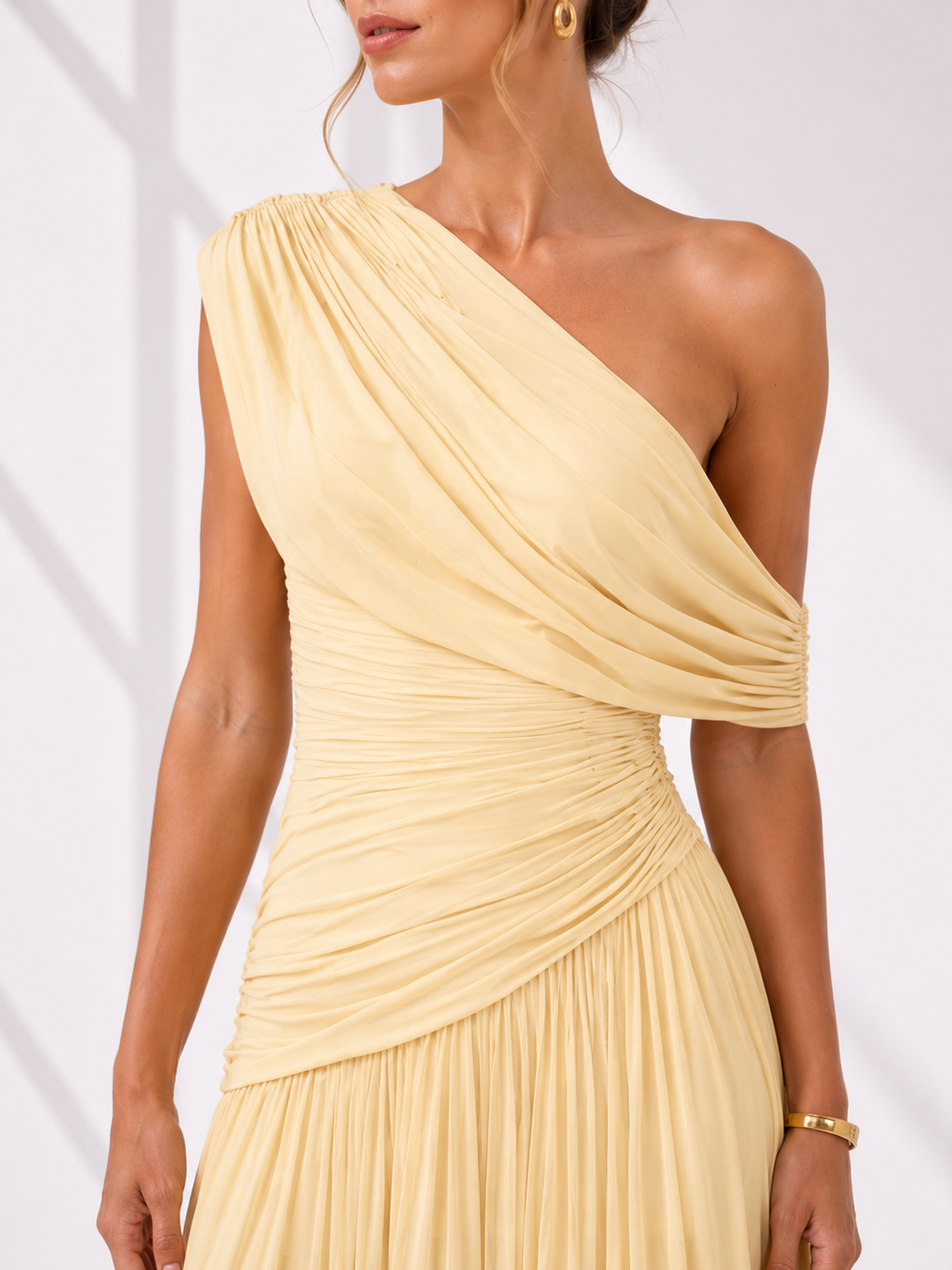 Woman wearing a one-shoulder beige dress against a white background
