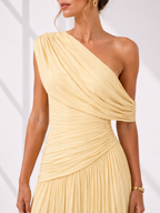 Woman wearing a one-shoulder beige dress against a white background