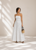 Woman wearing a strapless polka dot dress holding a woven handbag against a neutral background