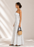 Woman in a white polka dot dress holding a woven bag against a neutral background