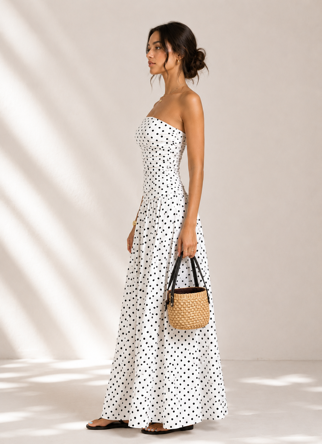 Woman in a white polka dot dress holding a woven bag against a neutral background