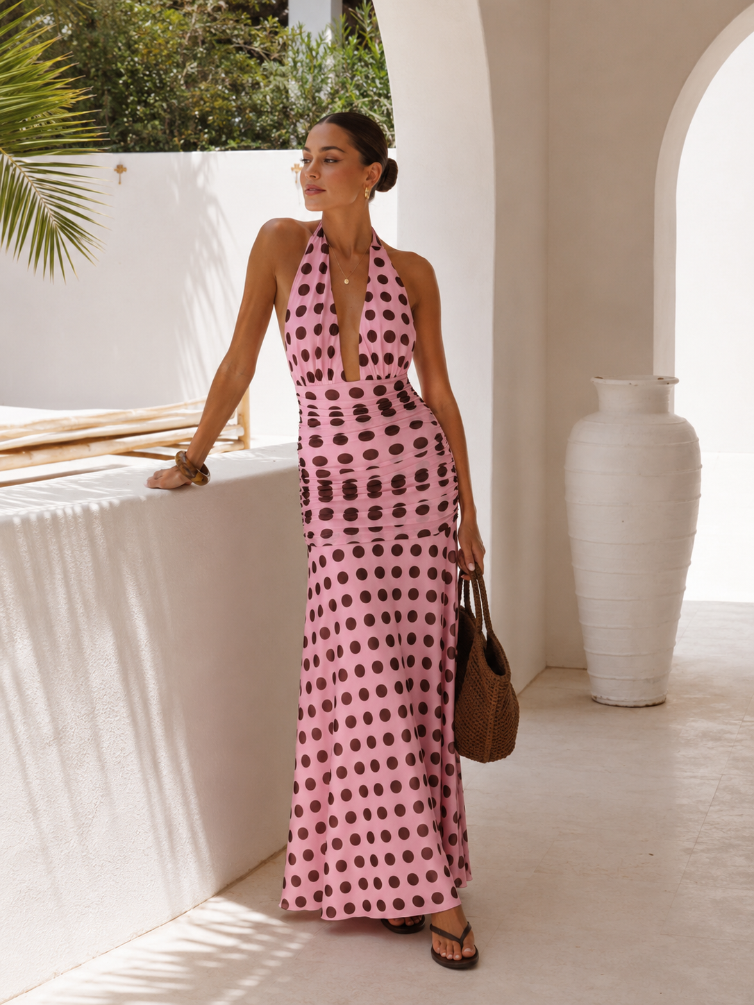 Woman in a pink polka dot dress standing in a sunlit outdoor setting.