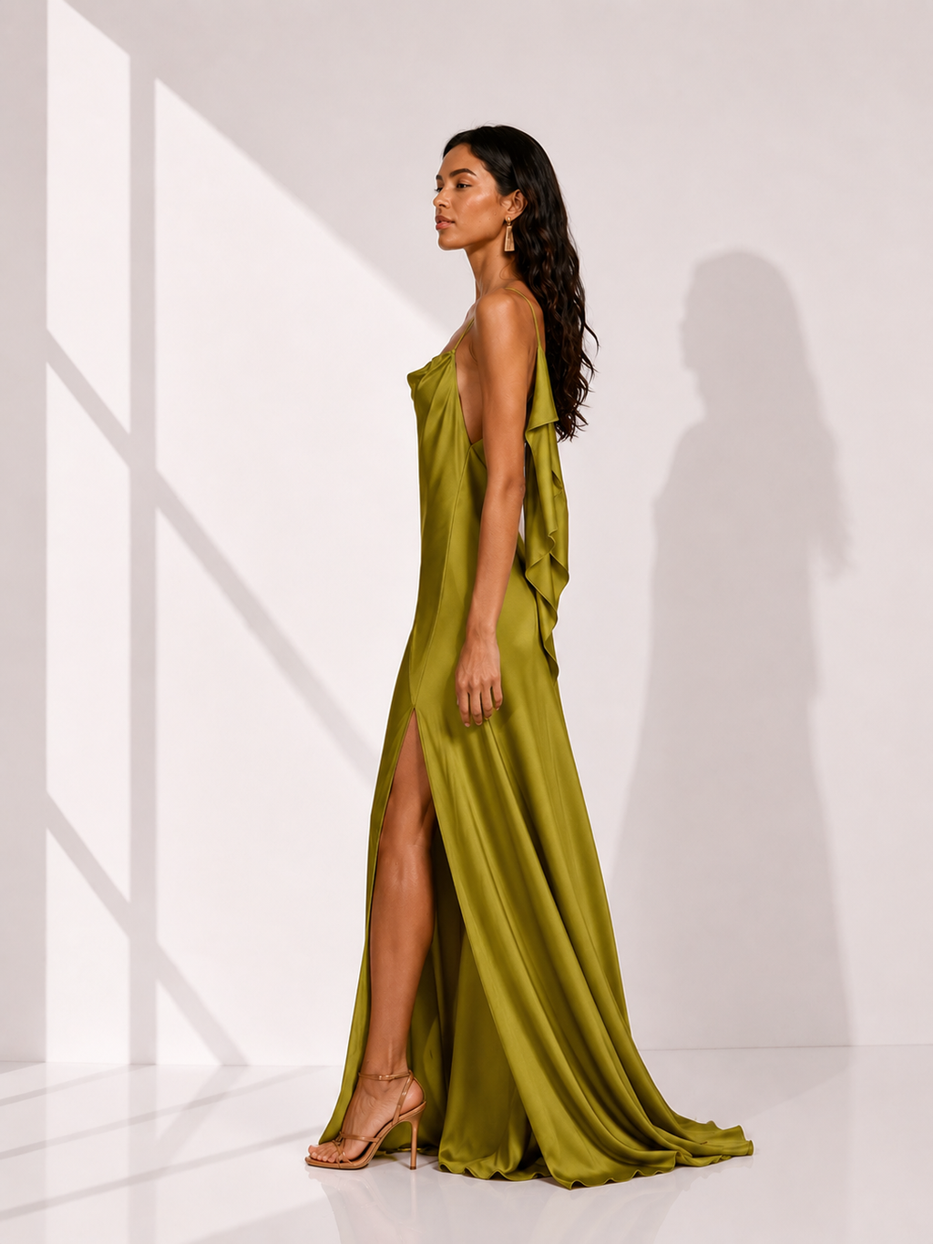 Woman wearing a green evening gown with a slit, standing in a bright room.