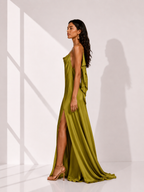 Woman wearing a green evening gown with a slit, standing in a bright room.