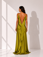 Woman wearing a green evening gown with a deep neckline and open back, standing against a white wall.