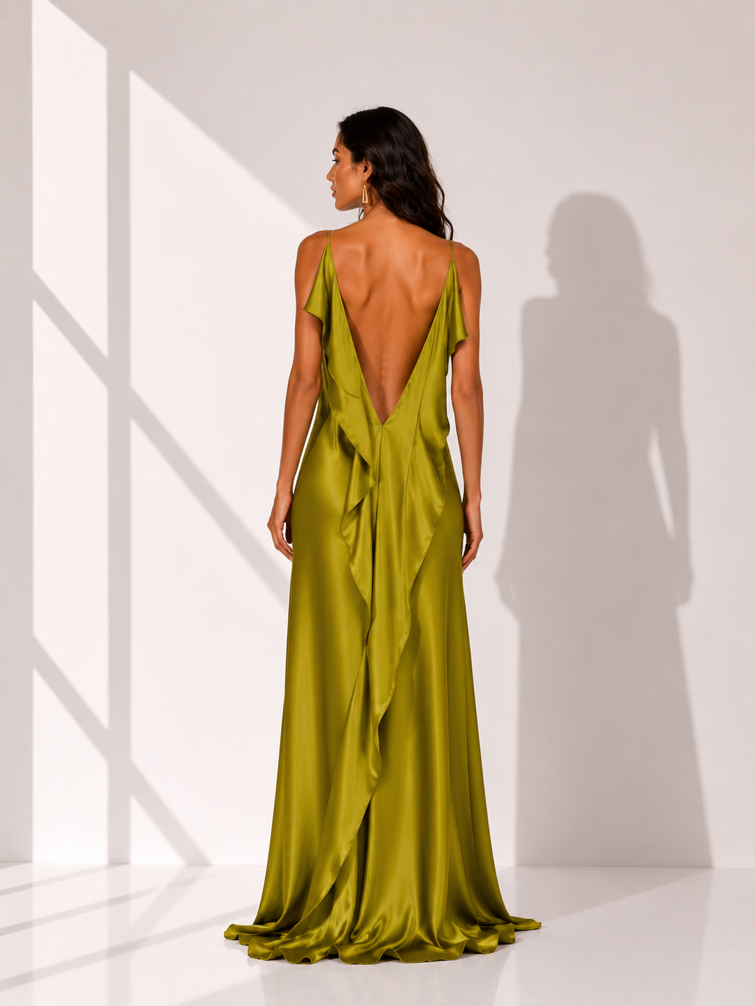 Woman wearing a green evening gown with a deep neckline and open back, standing against a white wall.