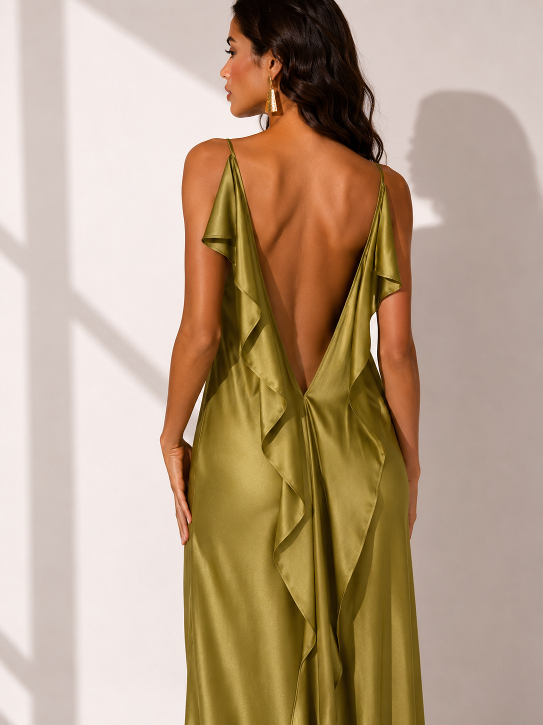 Woman wearing a green satin dress with a deep neckline and ruffled details, standing against a neutral background.