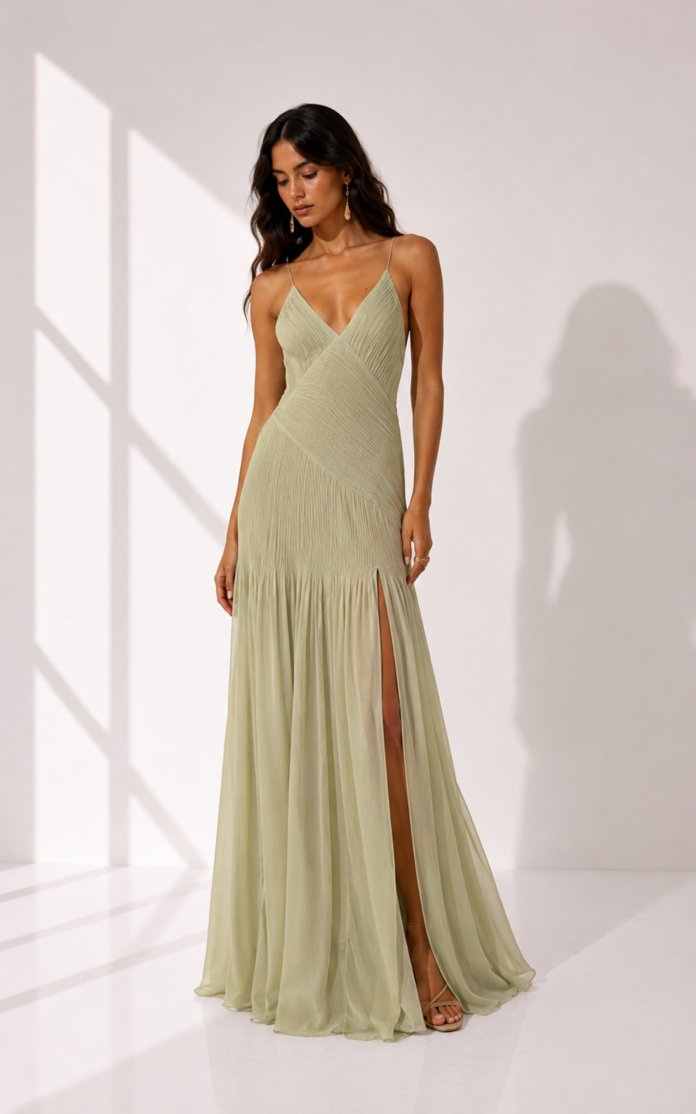 Woman wearing a light green evening gown with a slit on a white background