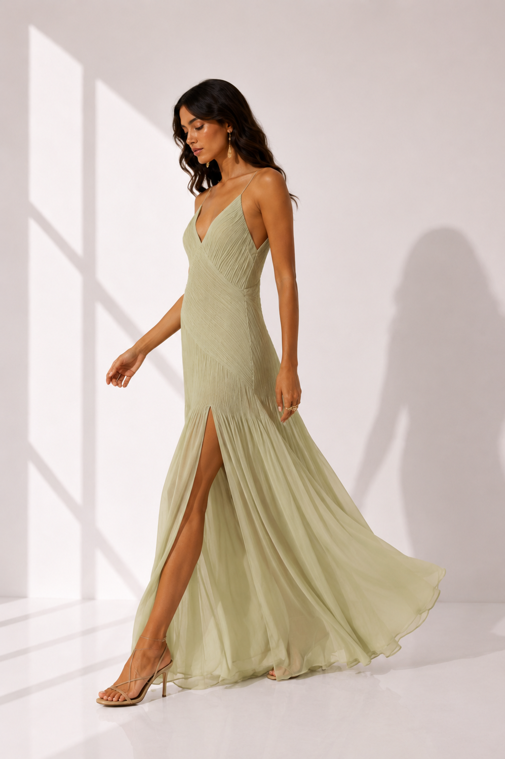 Woman wearing a light green evening gown with a slit on a white background