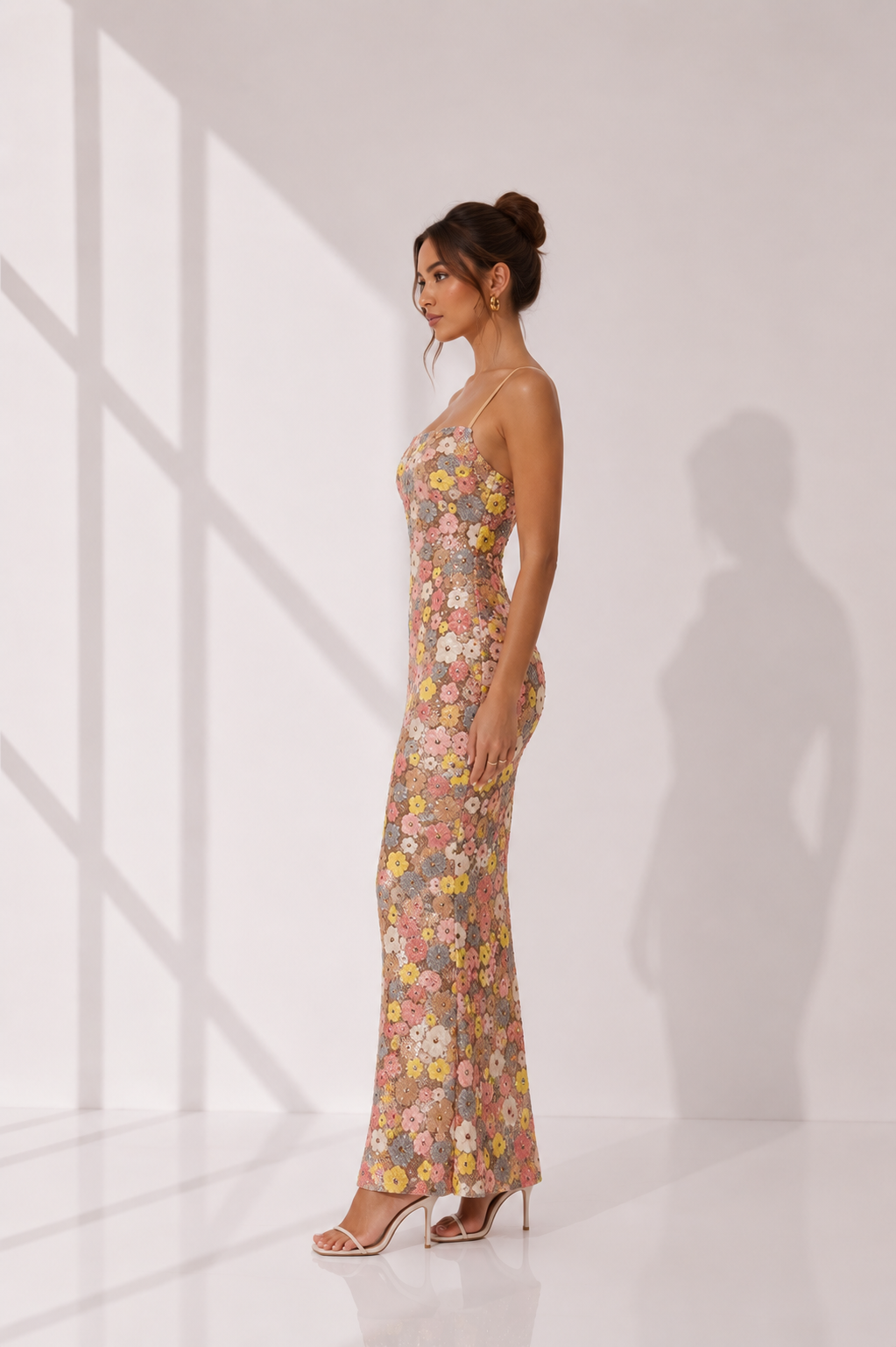 Woman wearing a floral dress standing in a well-lit room with sunlight casting shadows on the wall.