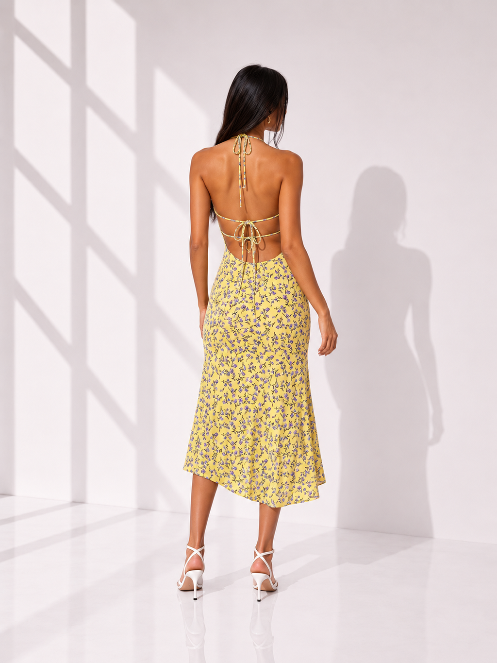 Woman wearing a yellow floral dress in a bright room with white walls.