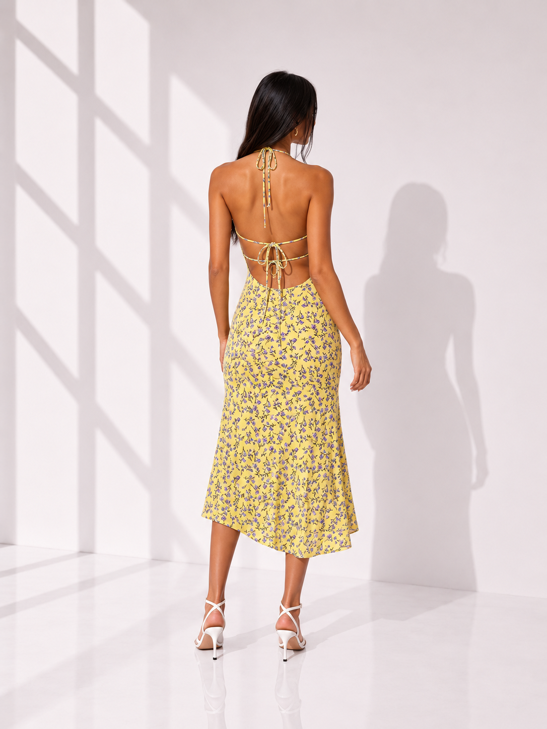 Woman wearing a yellow floral dress in a bright room with white walls.