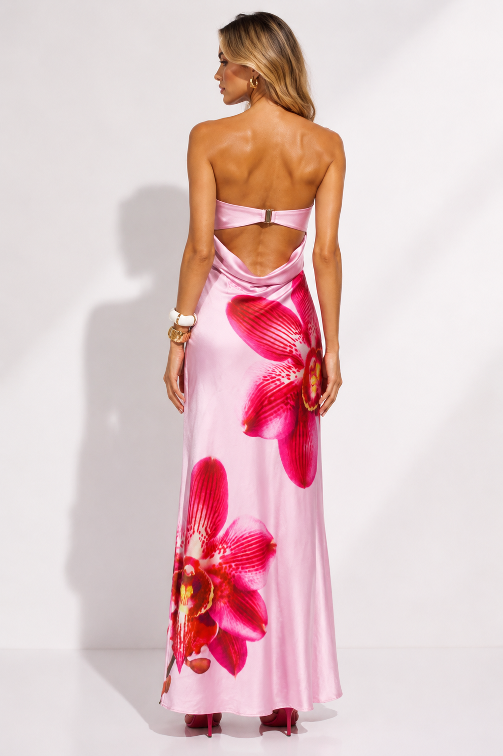 Woman wearing a pink strapless dress with large red floral patterns on a white background