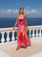 Woman in a pink floral dress standing on a balcony overlooking the ocean.