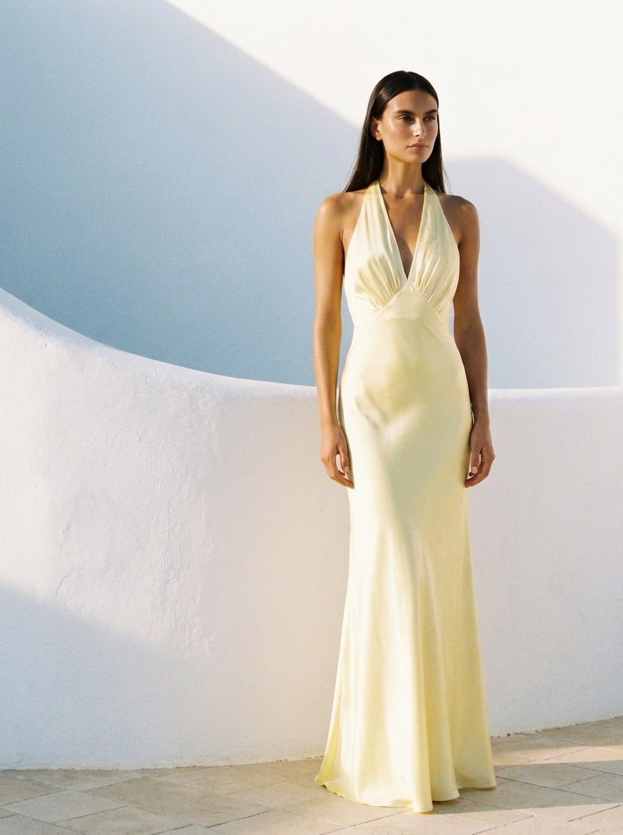 Woman in a light-colored evening gown standing against a white wall with blue sky.