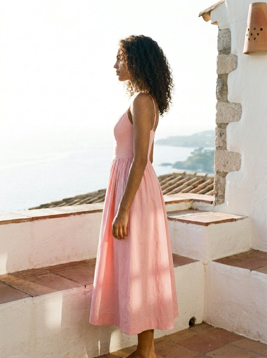 Woman in a pink dress standing on a balcony with a scenic view.