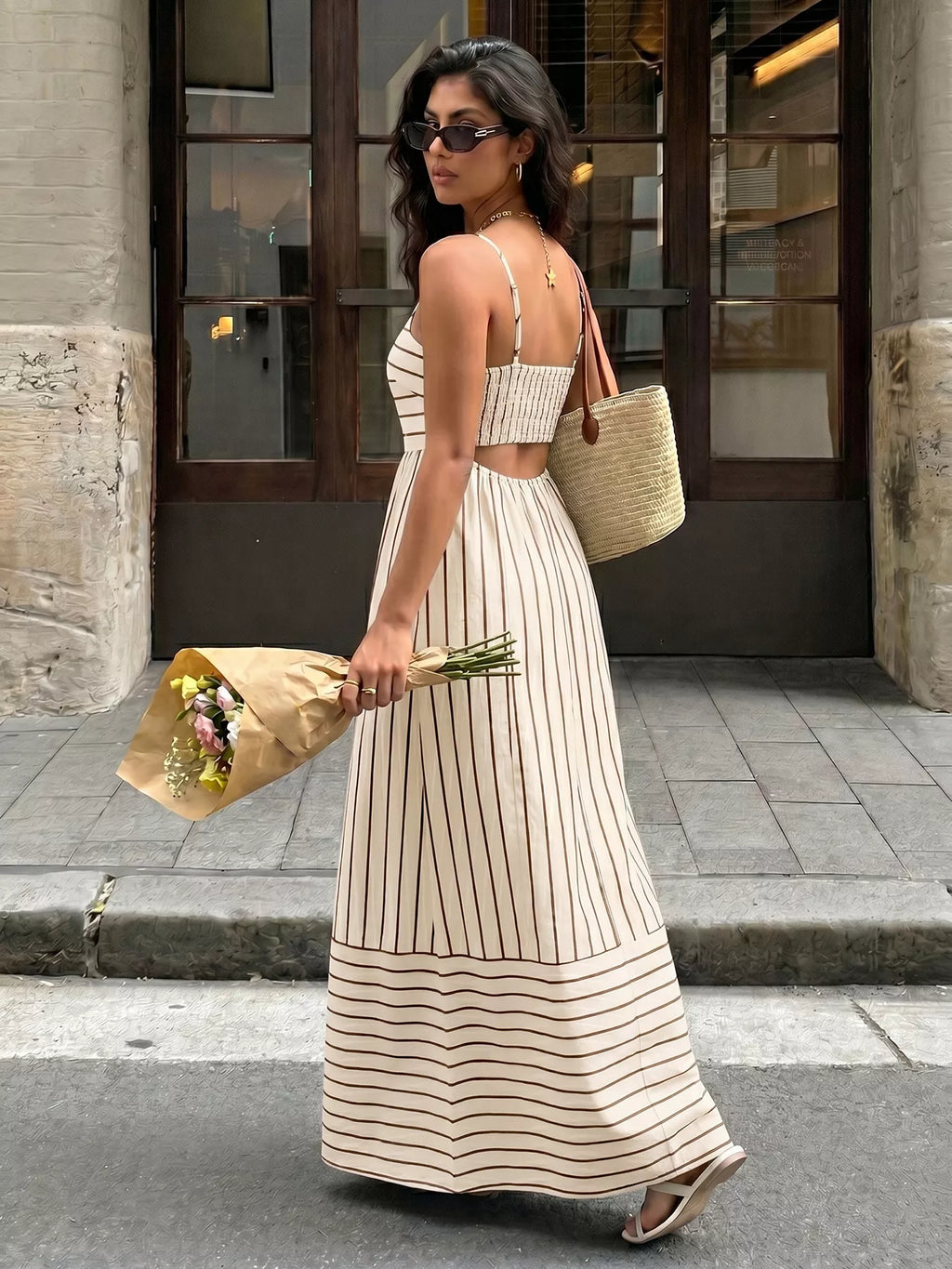 Woman in a long striped dress holding flowers on a city street.