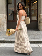 Woman in a long striped dress holding flowers on a city street.