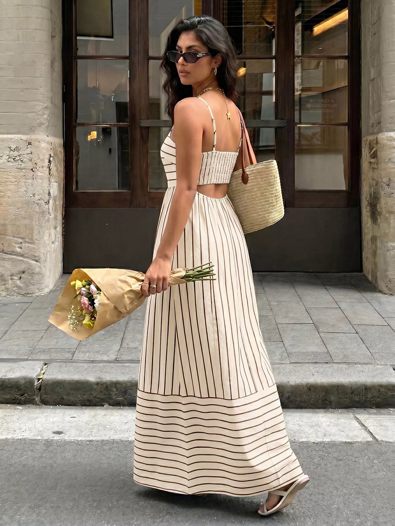 Woman in a long striped dress holding flowers on a city street.