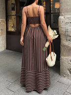 Woman in a brown and white striped dress holding flowers and a bag, standing on a street.