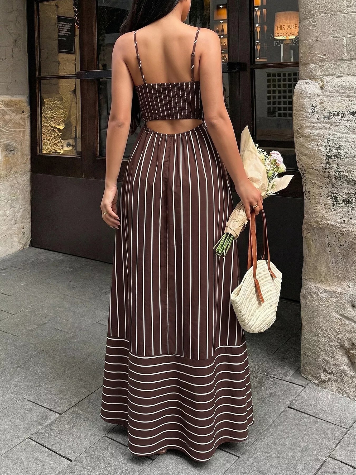 Woman in a brown and white striped dress holding flowers and a bag, standing on a street.