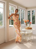 Woman wearing a floral dress in a bright room with white furniture and flowers.