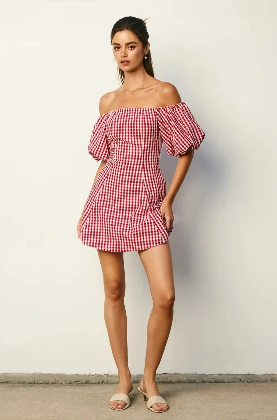 Woman wearing a red and white checkered off-shoulder dress against a plain background