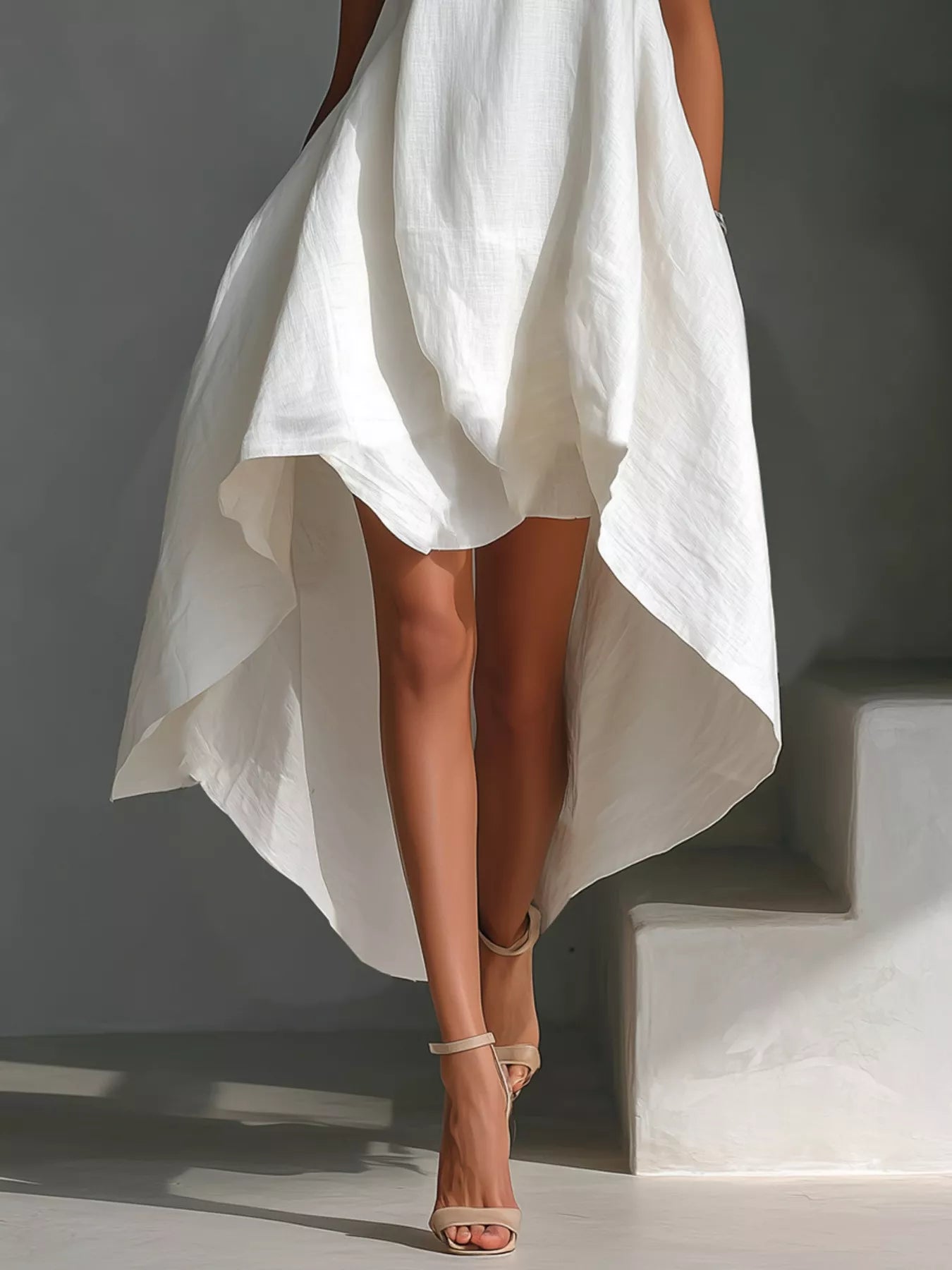 White dress with a high-low hemline worn by a person on a gray background