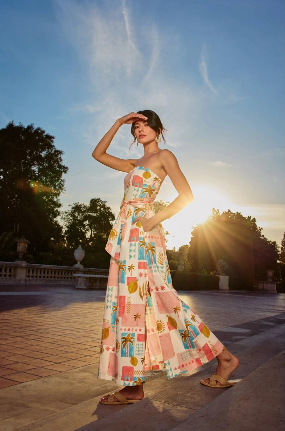 Woman in a colorful dress standing outdoors with trees and sunlight in the background