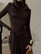Woman wearing a brown dress with a knot detail in a room setting.