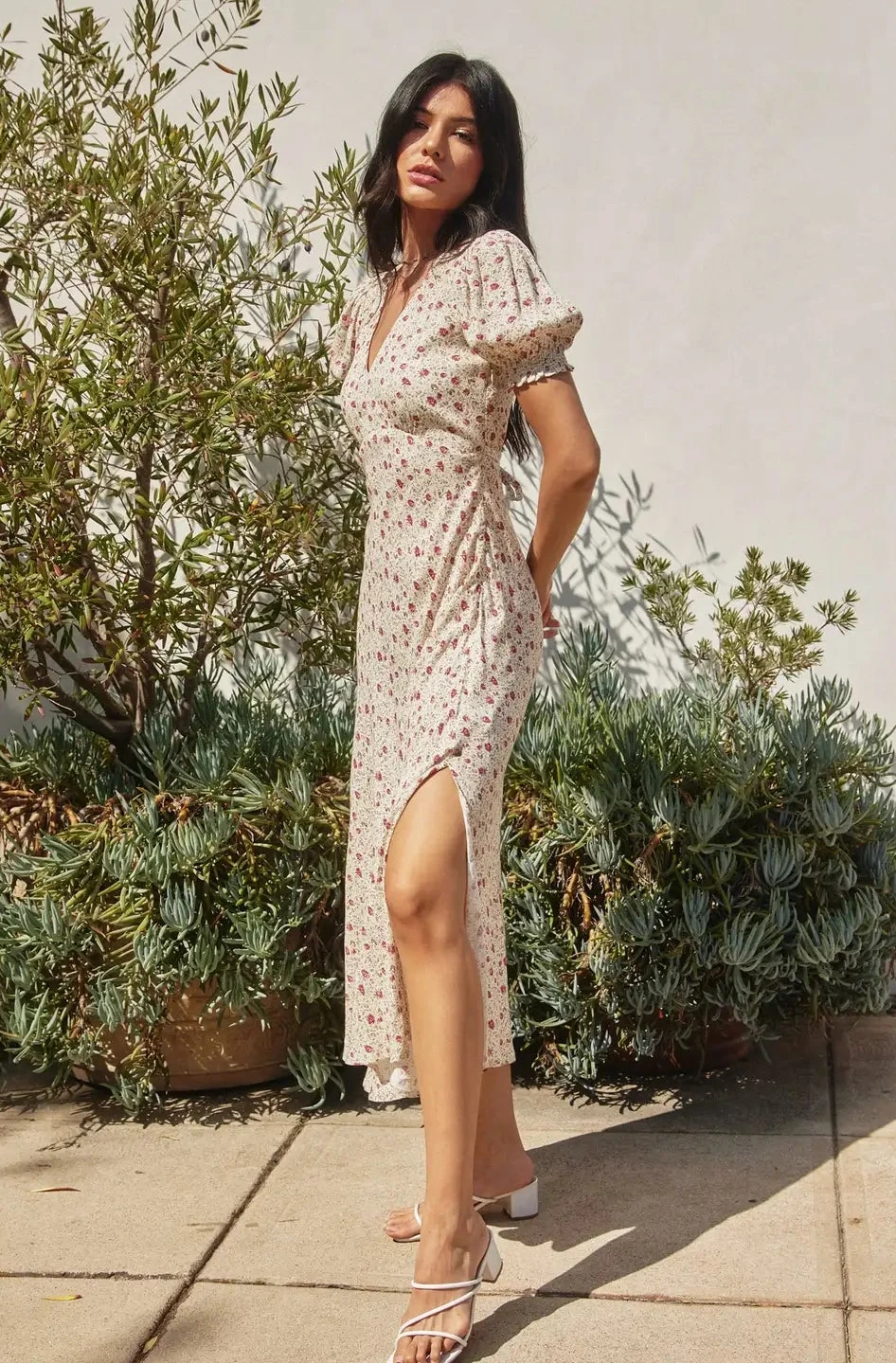Woman in a floral dress standing outdoors with plants in the background